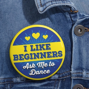 May include: A yellow and blue button with the text "I like beginners Ask Me to Dance" and three yellow hearts.