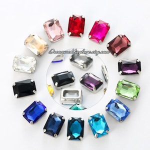 Può includere: Assortimento di 16 strass rettangolari in vari colori, tra cui nero, bianco, rosso, rosa, viola, blu, verde e trasparente. Gli strass sono incastonati in montature metalliche argentate.