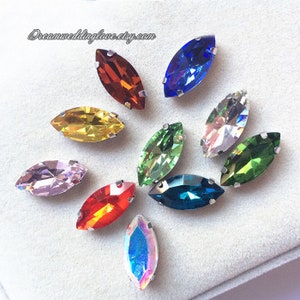 May include: Assortment of 10 marquise-shaped rhinestones in various colours, including red, orange, yellow, green, blue, and pink. The rhinestones have a silver-toned setting.