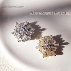 May include: Two silver and gold microencrusted zircon buttons in a starburst design.  The buttons are on a white surface.  Microencrusted Zircon Button.