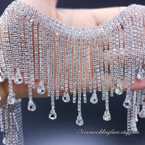 Peut inclure: Une bordure de frange en strass argent avec des strass en forme de goutte. La frange mesure environ 5 cm de long.