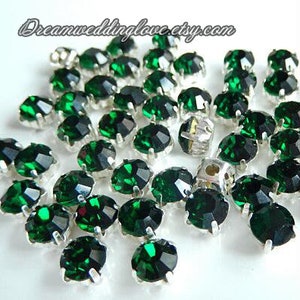 May include: A large quantity of emerald green rhinestones with silver settings. The rhinestones are scattered on a white surface.