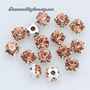 May include: A collection of 15 peach-colored round rhinestones with silver settings. The rhinestones are scattered on a white surface.
