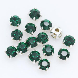 May include: Assortment of green rhinestones with silver settings. The rhinestones are round and have a faceted design.