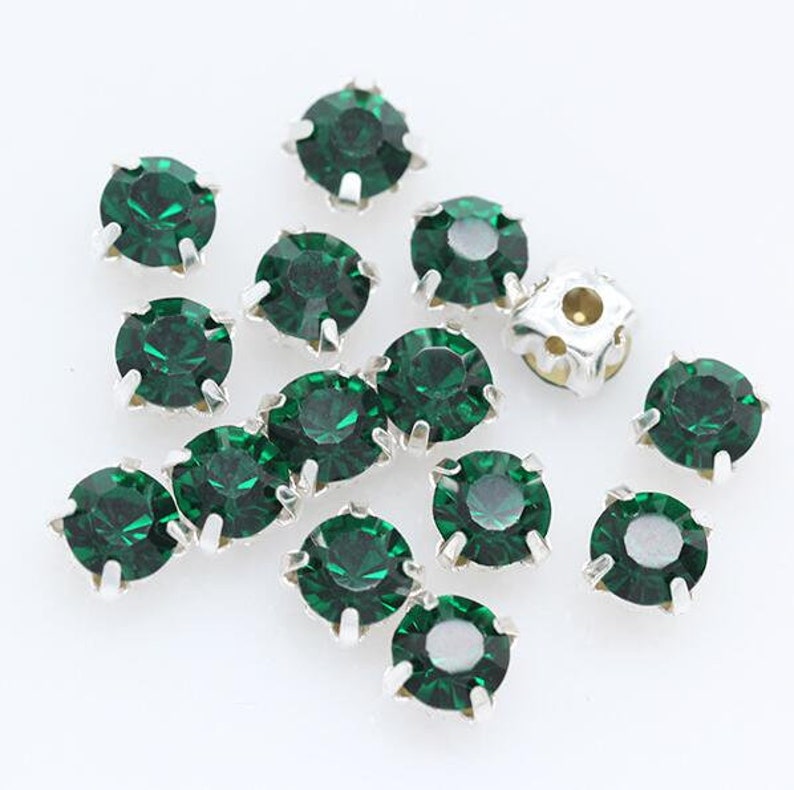 May include: Assortment of green rhinestones with silver settings. The rhinestones are round and have a faceted design.