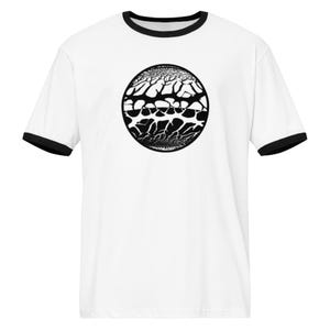 May include: A white ringer t-shirt with black trim on the collar and sleeve cuffs. The center of the chest features a circular graphic containing a black and white abstract pattern resembling cracked earth or branching organic textures in a sphere.