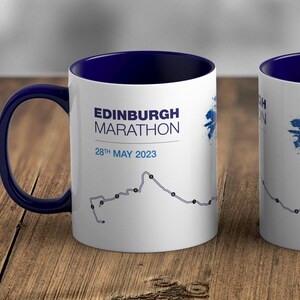 May include: White ceramic mug with a blue rim and handle. The mug features a graphic of the Edinburgh Marathon route with the text "EDINBURGH MARATHON 28th MAY 2023".