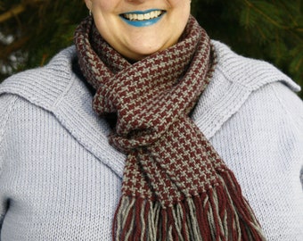 Könnte beinhalten: Eine Frau mit kurzen, roten Haaren trägt einen helllila Strickpullover und einen braunen und grauen gemusterten Schal mit langen Fransen. Sie lächelt und hat blauen Lippenstift.