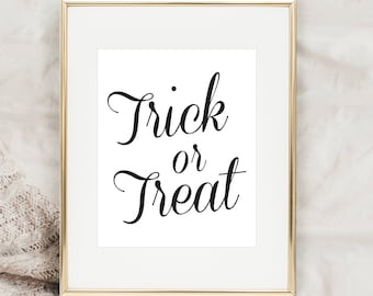 Puede incluir: Una impresión enmarcada en oro con el texto "Trick or Treat" en fuente cursiva negra sobre un fondo blanco.