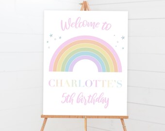Könnte beinhalten: Ein weißes Schild auf einer Holzstaffelei mit einem pastellfarbenen Regenbogen und dem Text "Welcome to". Darunter steht "CHARLOTTE'S 5th birthday" in einem weichen, hellvioletten Farbton. Kleine Sterne sind um den Regenbogen herum verstreut.