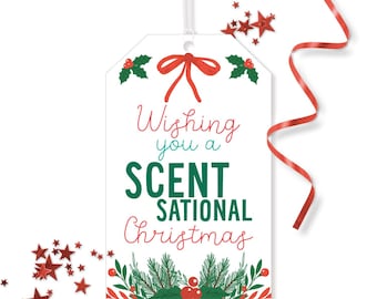 May include: A white gift tag with a red bow, holly accents, and the text "Wishing you a SCENT-SATIONAL Christmas" in red and green. Red star-shaped confetti and a red ribbon are scattered around the tag.