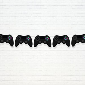 Puede incluir: Cinco mandos de videojuegos negros con botones de colores están enhebrados en una fila contra un fondo de pared de ladrillo blanco.