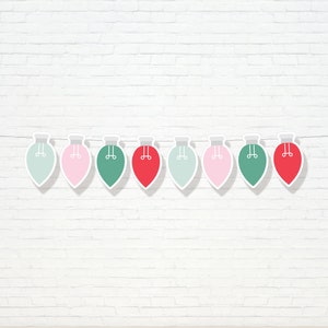 Puede incluir: Una cadena de nueve luces de Navidad de papel en colores alternados rojo, verde y rosa. Las luces están colgadas en una pared de ladrillo blanco.