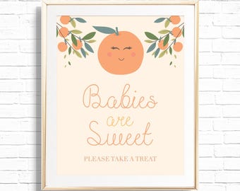 May include: A framed print with a light peach background. The print features a smiling orange with leaves and the text "Babies are Sweet, Please Take a Treat" in a whimsical font. The frame is a light wood color.