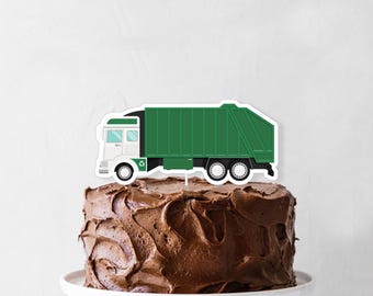 May include: A chocolate cake with a green and white garbage truck cake topper. The truck has a recycling symbol on the side.