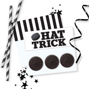 May include: A white card with black stripes and the text "HAT TRICK" with a black hockey puck graphic. Three black Oreo cookies are on the card.