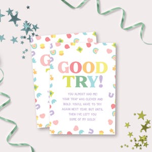 Könnte beinhalten: Eine weiße Karte mit einem Regenbogen-, Kleeblatt- und Hufeisenmuster. Die Karte sagt "GOOD TRY!" in bunten Buchstaben. Der Text darunter lautet "You almost had me! Your trap was clever and bold. You'll have to try again next year, but until then I've left you some of my gold!"
