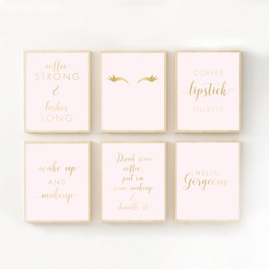 May include: Six pink and gold framed prints with motivational quotes about coffee and makeup. The quotes include "Coffee Strong & Lashes Long", "Drink Some Coffee, Put On Some Makeup & Handle It", "Wake Up And Makeup", "Coffee Lipstick Hustle", "Hello Gorgeous", and a graphic of two eyelashes.
