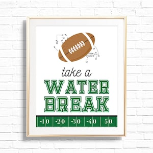 Op de afbeelding: Ingelijste print met een voetbal en spelschema's. De tekst "take a WATER BREAK" staat in groene blokletters. Onderaan staat een groene veldafbeelding met yardlijnen. De print zit in een licht houten frame.