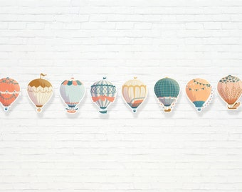 Puede incluir: Una fila de nueve globos aerostáticos coloridos con varios patrones y diseños. Los globos están dispuestos en línea contra un fondo de pared de ladrillo blanco.