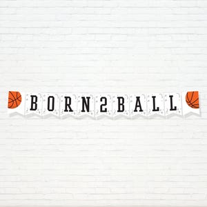 Może przedstawiać: Biały baner z czarnymi literami z napisem "BORN 2 BALL" jest wyświetlany na tle białej ceglanej ściany. Baner ma grafikę koszykówki na każdym końcu. Piłki do koszykówki są pomarańczowe z czarnymi liniami.