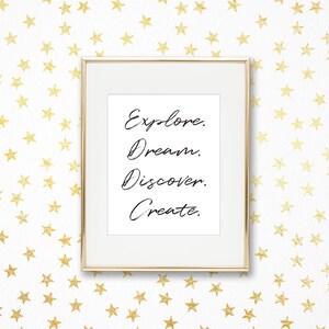 Pode incluir: Uma impressão emoldurada em dourado com as palavras "Explorar. Sonhar. Descobrir. Criar." em um fundo branco. A impressão é cercada por um fundo branco com um padrão de estrelas douradas.
