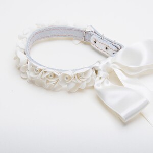 Può includere: Collare per cani bianco con un fiocco di raso bianco e una fila di fiori di stoffa bianchi con accenti di perle.