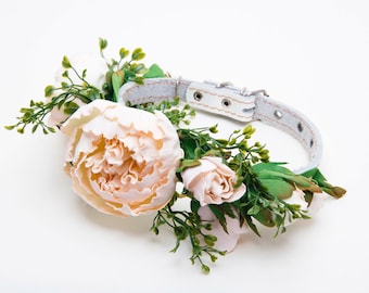 Puede incluir: Un collar de perro de cuero blanco adornado con un delicado arreglo floral con peonías rosas y vegetación.