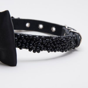 May include: Black dog collar with a satin bow and a beaded section. The collar is made of black leather and has a silver-colored buckle and eyelets. The beaded section is made of small, black beads.