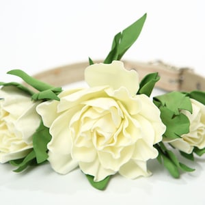 Puede incluir: Un collar de perro de cuero blanco con tres flores de tela blancas y hojas verdes.