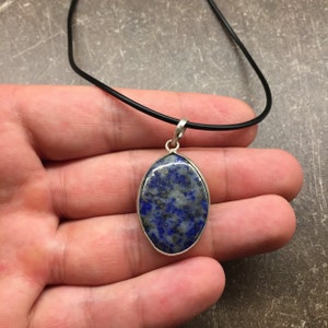 May include: A silver pendant necklace with a blue and white oval lapis lazuli stone. The necklace is on a black cord.