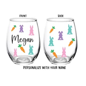 May include: Two clear stemless wine glasses with a personalized name, "Megan", on the front glass. The glasses are decorated with pastel colored bunnies and carrots.