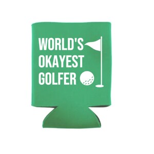Op de afbeelding: Groene koelbox voor blikjes met de tekst "WORLD'S OKAYEST GOLFER" in wit. Een witte golfbal en vlag bevinden zich aan de rechterkant van de koelbox.