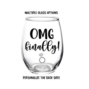 Peut inclure: Un verre &agrave; vin en verre transparent avec le texte "OMG finally!" et une bague en argent avec un diamant. Le verre est pour un mariage ou une f&ecirc;te de fian&ccedil;ailles.