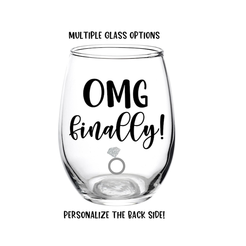 Peut inclure: Un verre &agrave; vin en verre transparent avec le texte "OMG finally!" et une bague en argent avec un diamant. Le verre est pour un mariage ou une f&ecirc;te de fian&ccedil;ailles.