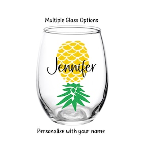 May include: A clear glass wine glass with a yellow pineapple design and the name "Jennifer" printed on it.  The pineapple has green leaves.