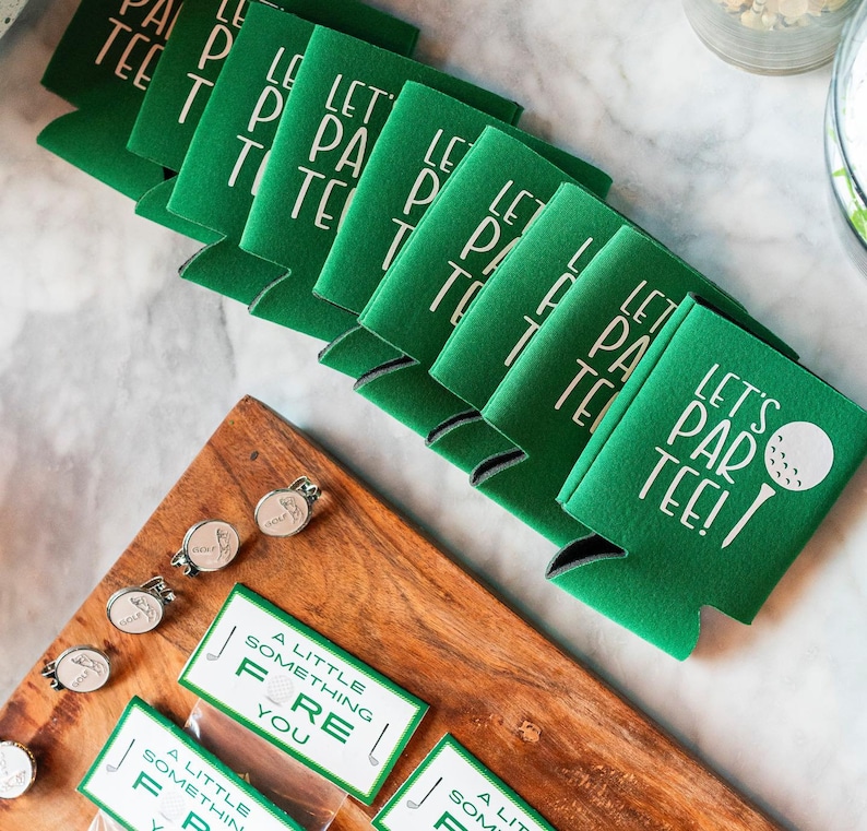 May include: A stack of green and white golf-themed beverage insulators with the text "Let's Par Tee!" printed on them. A golf ball and club are pictured on the top insulator.