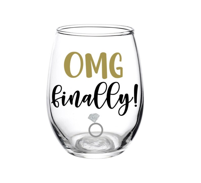 Peut inclure: Un verre &agrave; vin en verre transparent avec le texte "OMG finally!" en lettres noires et un graphique de bague de fian&ccedil;ailles en diamant dor&eacute;.