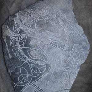 May include: A gray slate carving of a deer with antlers, surrounded by a Celtic knot design. The carving is signed "Ann Smith"