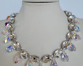 May include: A silver necklace with large, clear, iridescent crystal stones. The necklace has a row of oval-shaped stones with smaller teardrop-shaped stones hanging from them.