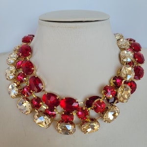May include: A gold tone statement necklace with large red and clear faceted crystal stones. The necklace is layered with two rows of crystals.
