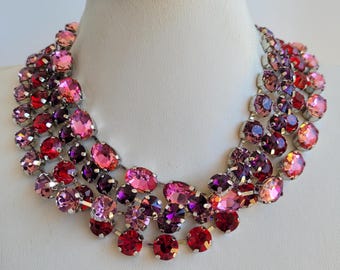 Peut inclure: Un collier spectaculaire orné de strass roses, rouges et violets, disposés en couches sur un support argenté. Le collier est présenté sur un buste de mannequin blanc. Les pierres sont de formes variées.