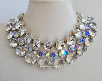 May include: A multi-layered crystal necklace with clear, faceted stones. The necklace is made of silver-toned metal and features three rows of stones, with the top row being the smallest and the bottom row being the largest.