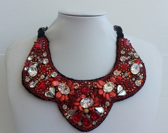 Peut inclure: Un collier ras de cou en cristal rouge et transparent avec un dos noir. Le collier est composé de cristaux et de perles de différentes tailles et formes.