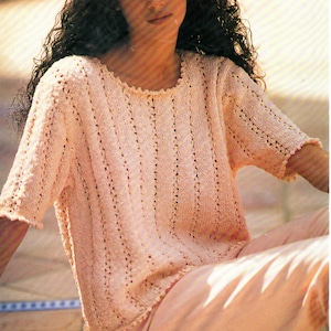 May include: A pale pink crocheted top with a round neckline and short sleeves. The top features a delicate openwork pattern.