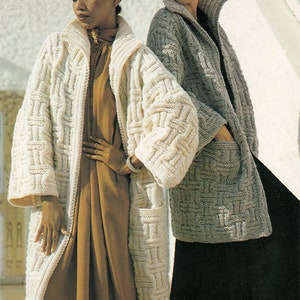 Puede incluir: Dos mujeres con cárdigans de punto largos. La mujer de la izquierda lleva un cárdigan blanco con un vestido marrón y una boina blanca. La mujer de la derecha lleva un cárdigan gris con una falda negra y una boina negra.