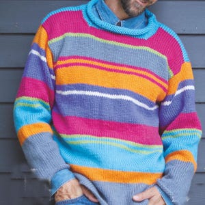 Puede incluir: Un suéter a rayas de colores en tonos rosa, naranja, azul y morado. El suéter tiene un cuello alto enrollado y mangas largas. Se lleva una camisa vaquera debajo.