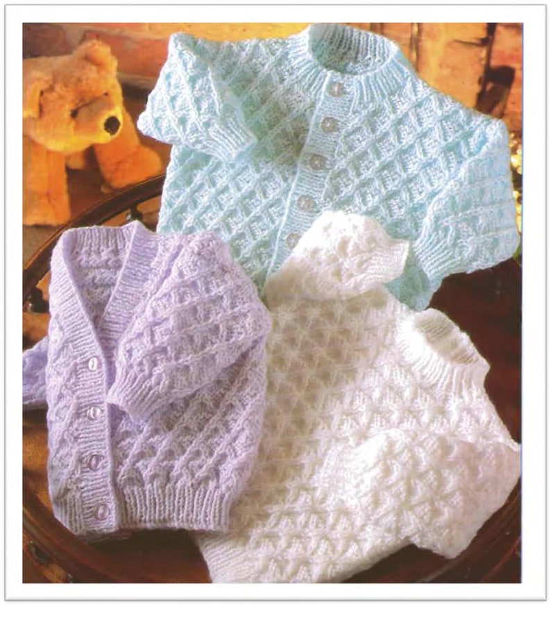 May include: Three knitted baby cardigans in different colors: light blue, lavender, and white. The cardigans have a button-up front and a diamond-shaped stitch pattern.