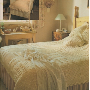 May include: A white crocheted bedspread with a cable knit pattern and a white crocheted pillow on a bed with a wooden headboard. The bedspread is on a bed with a white ruffle.