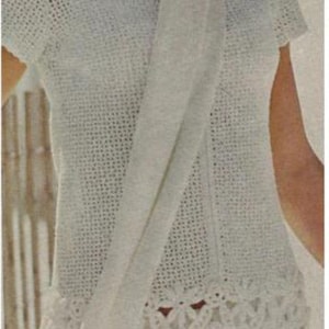 以下が含まれることがあります： レースの縁取りと、それに合わせた白いスカーフが付いた白いクロシェ編みドレス。ドレスは半袖で、丸首です。